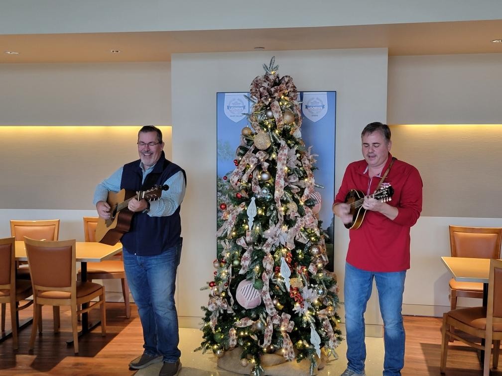 two men play instruments beside a christmas tree