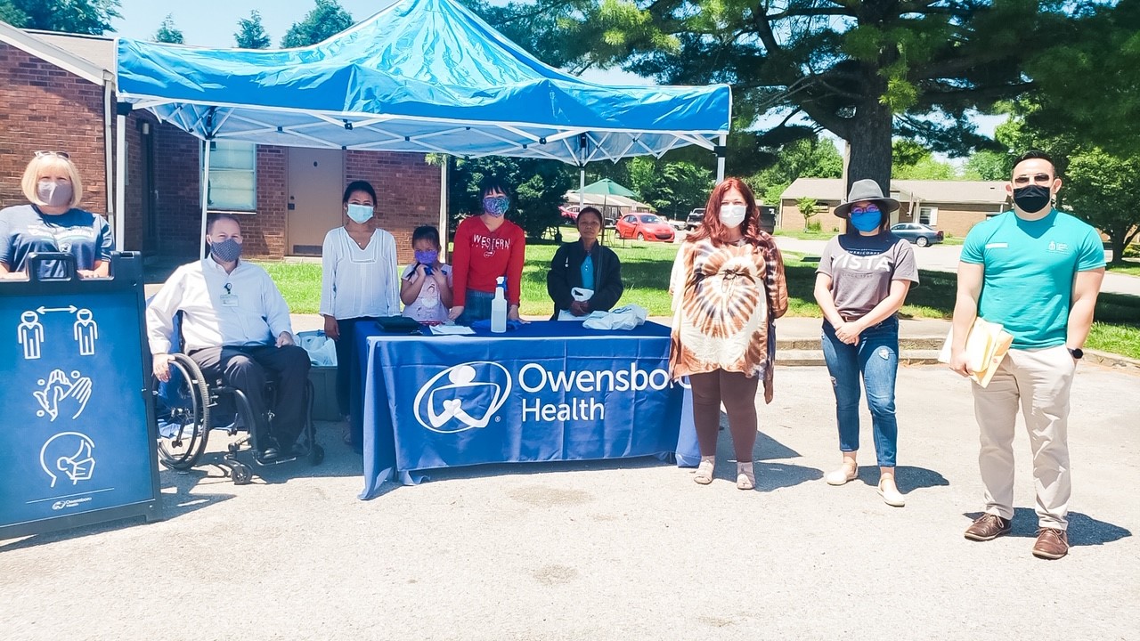 team members pose for a photo standing in front of an owensboro health booth
