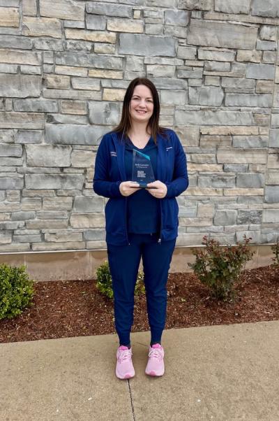 brunette woman in blue scrubs holds an award