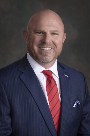 headshot of a bald white man in a suit