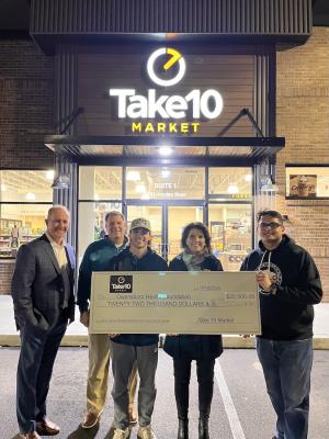 five people hold a giant check outside a convenient store