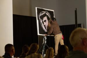 An artist paints a portrait of Elvis in front of a crowd